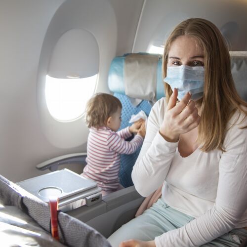 Frau sitzt mit Kleinkind im Flugzeug mit medizinischer Maske